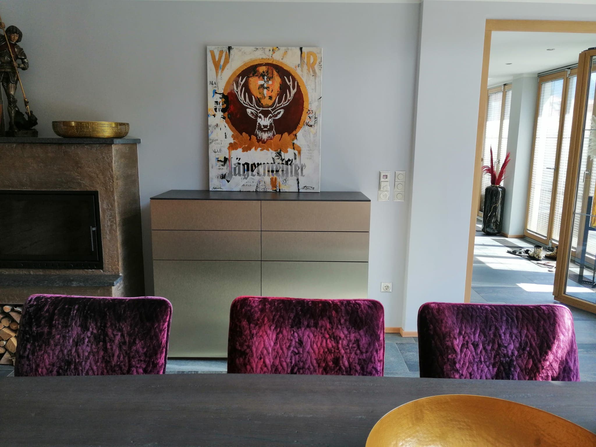 Sideboard mit Goldfinish neben dem Kamin, mit Kunstwerk und samtenen Stühlen