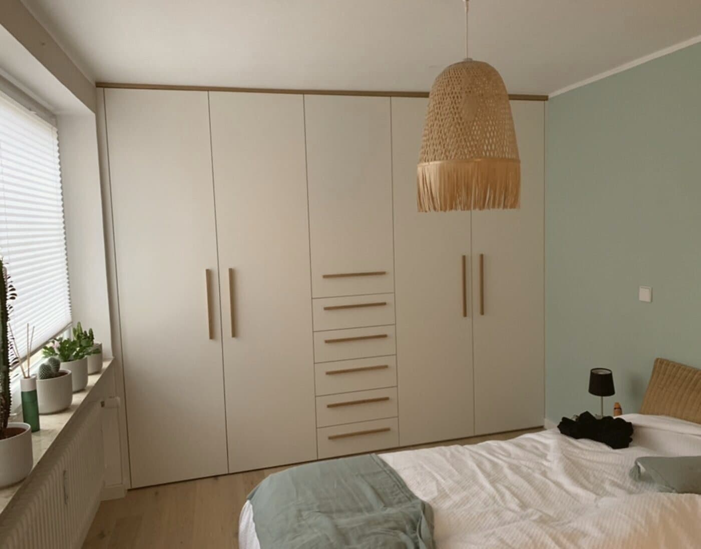 Floor-to-ceiling fitted wardrobe in the bedroom with cream fronts and wooden handles